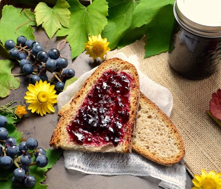 An overhead shot of the purple concord grape jelly spread over a slice of whole wheat bread.