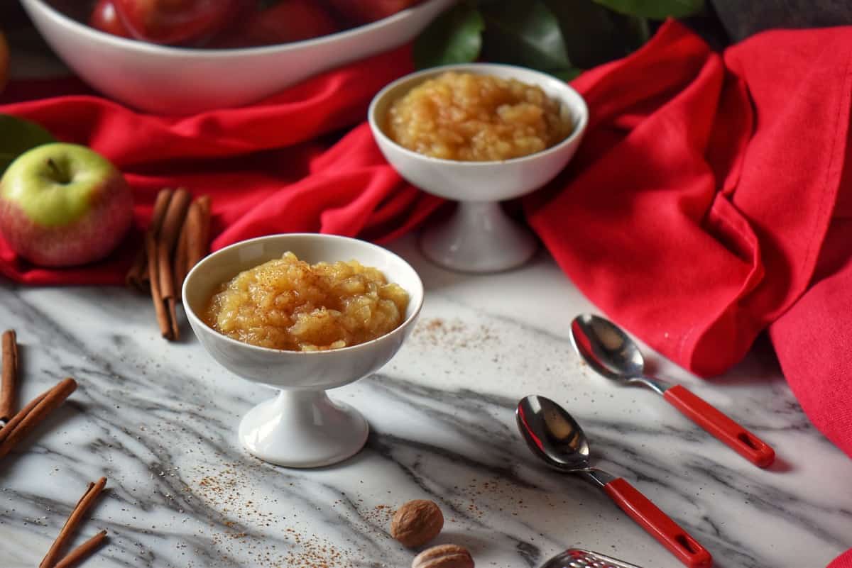 Chunky applesauce shown with apples and cinnamon sticks.