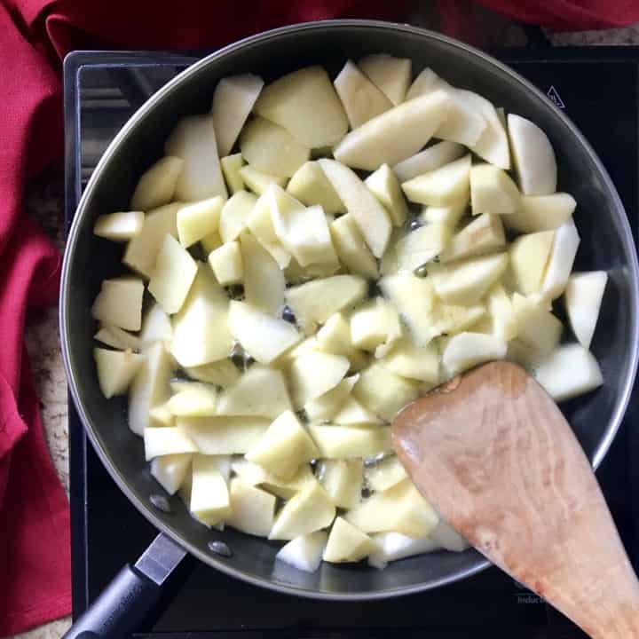 Chopped apples in a sauce pan being stirred with a wooden spoon.