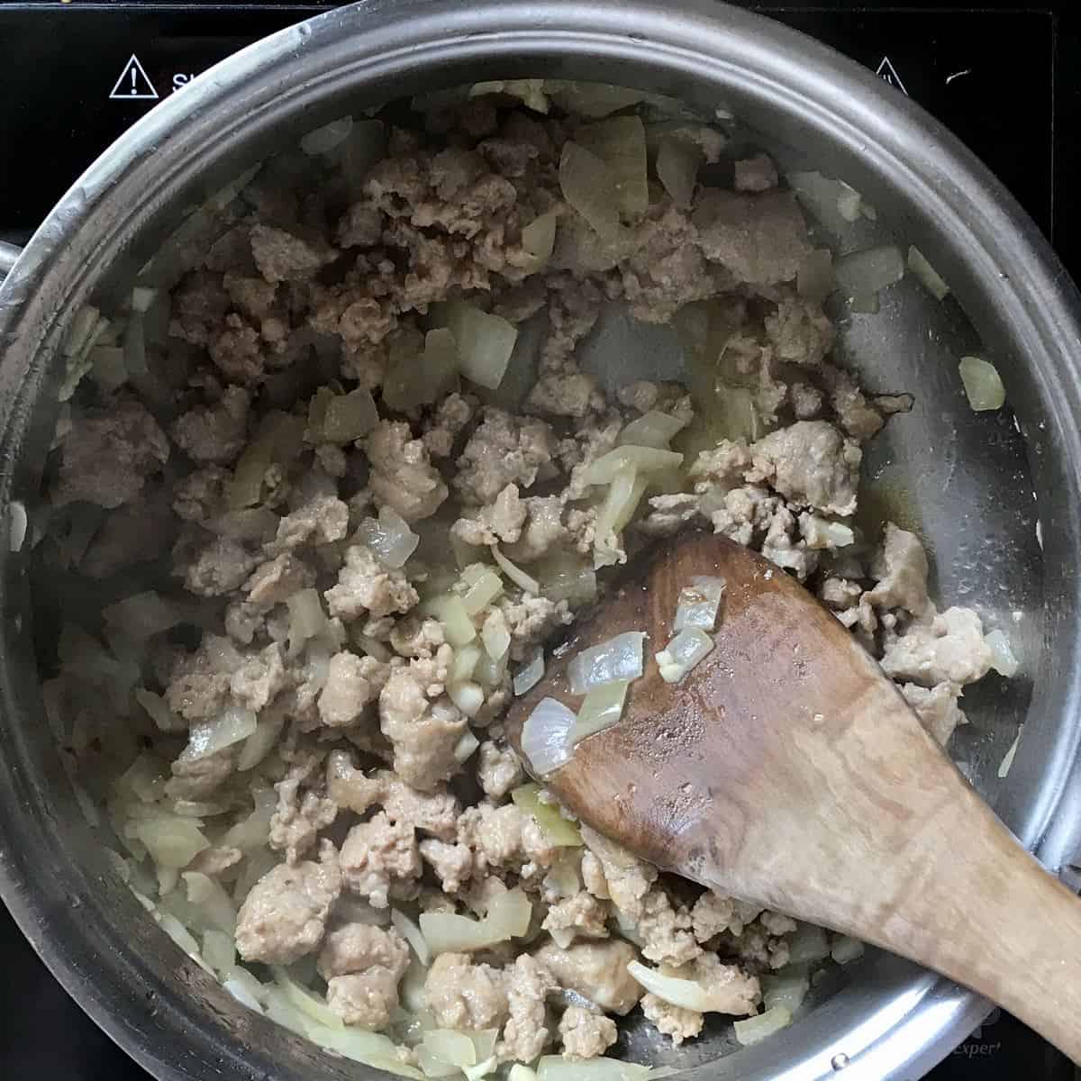 Italian sausage in the process of being sauteed in a large stockpot.