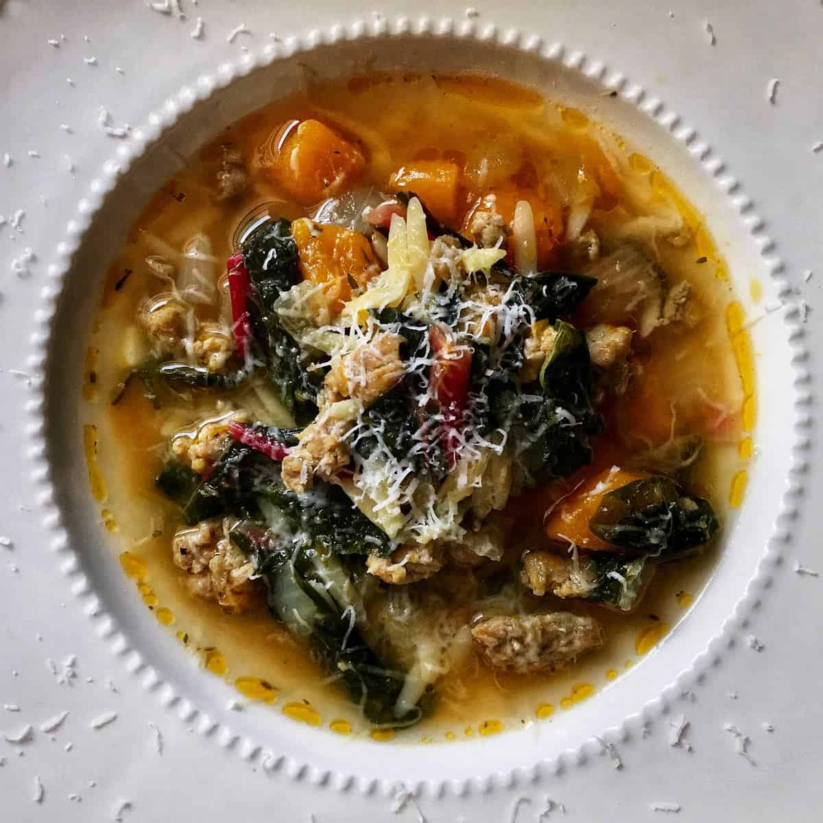 An overhead photo of Italian sausage squash soup and swiss chard with grated cheese