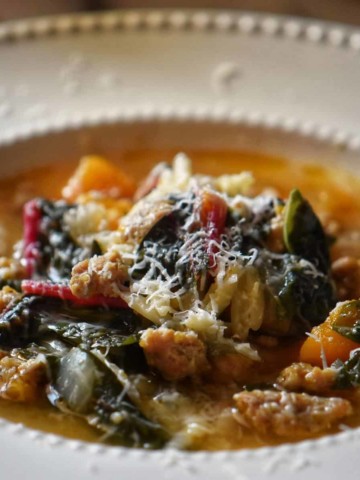 Italian Sausage Squash Soup with swiss chard in a white bowl.