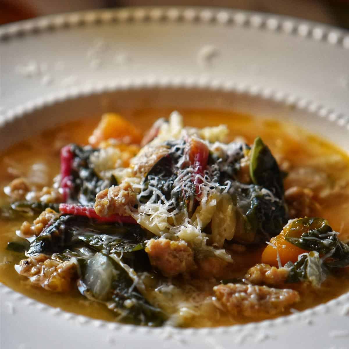 Italian Sausage Squash Soup with swiss chard in a white bowl.