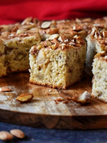 A few apple squares on a wooden board, surrounded by a few raw almonds.