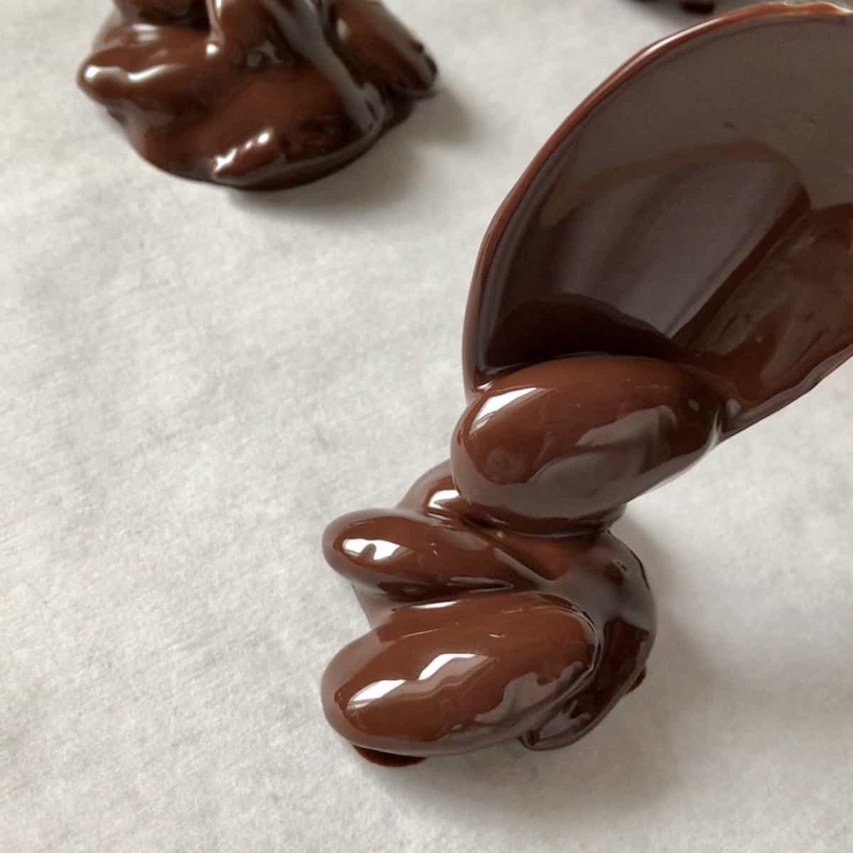 Choclate covered almonds being dropped on parchment paper. 