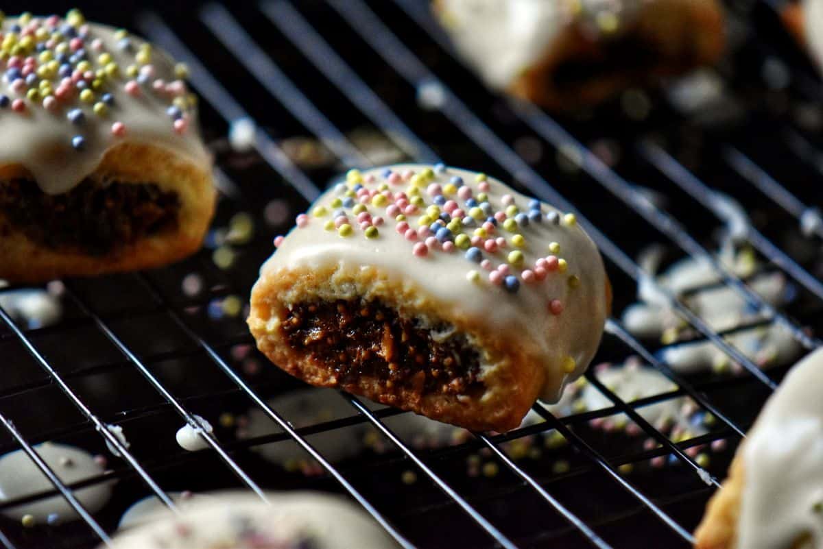 Cuccidati with white icing and sprinkles on a cooling rack.