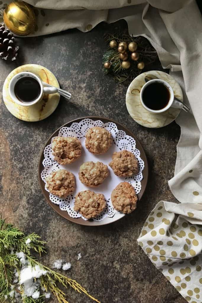 An overhead shot of the brutti and buoni cookies on a small plate, surrounded by 2 espressos and Christmas decorations.