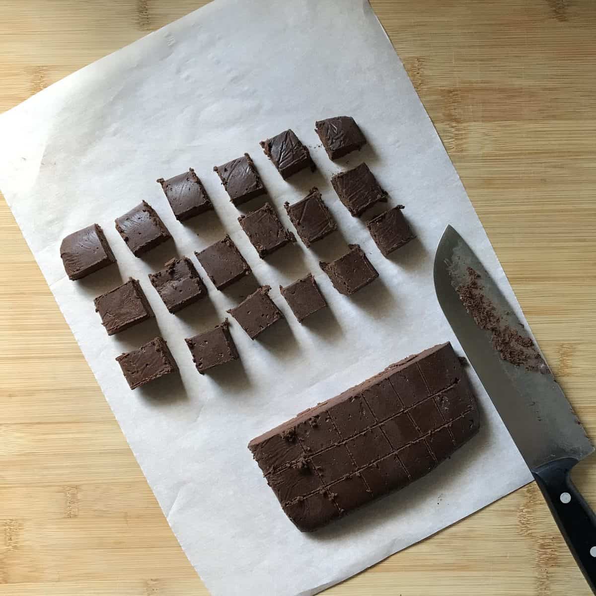 Chocolate crinkle dough is being cut into small squares, ready to be rolled. 