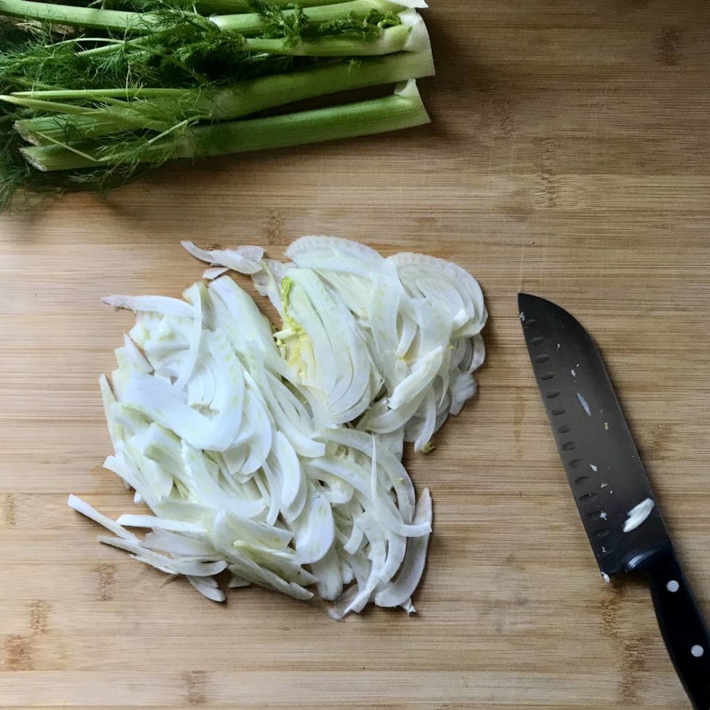 Thinly sliced fennel on a wooden board.