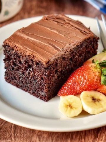 Chocolate cake with ganache frosting on a white plate.