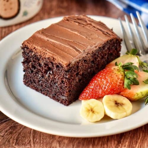 Chocolate cake with ganache frosting on a white plate.