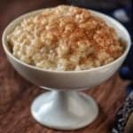 Arborio rice pudding sprinkled with cinnamon powder in a white dessert dish.