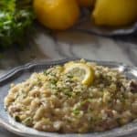 Mushroom Risotto in a pewter plate, topped with chopped parsley and a slice of lemon.