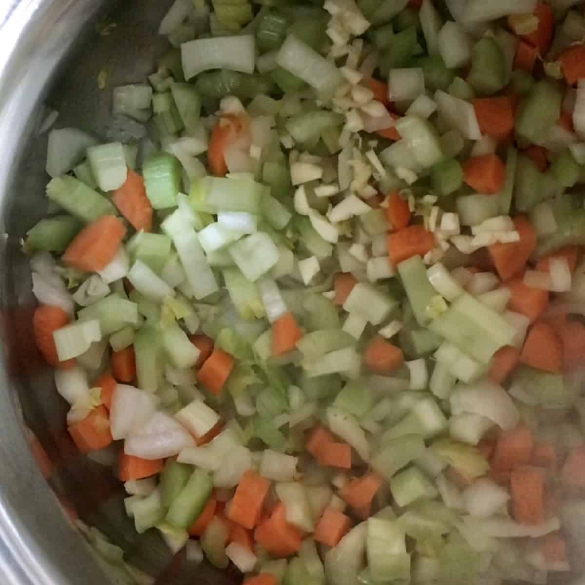 The cut up vegetables (carrots, celery, onion) for the bean soup are being sauteed in a large pot.
