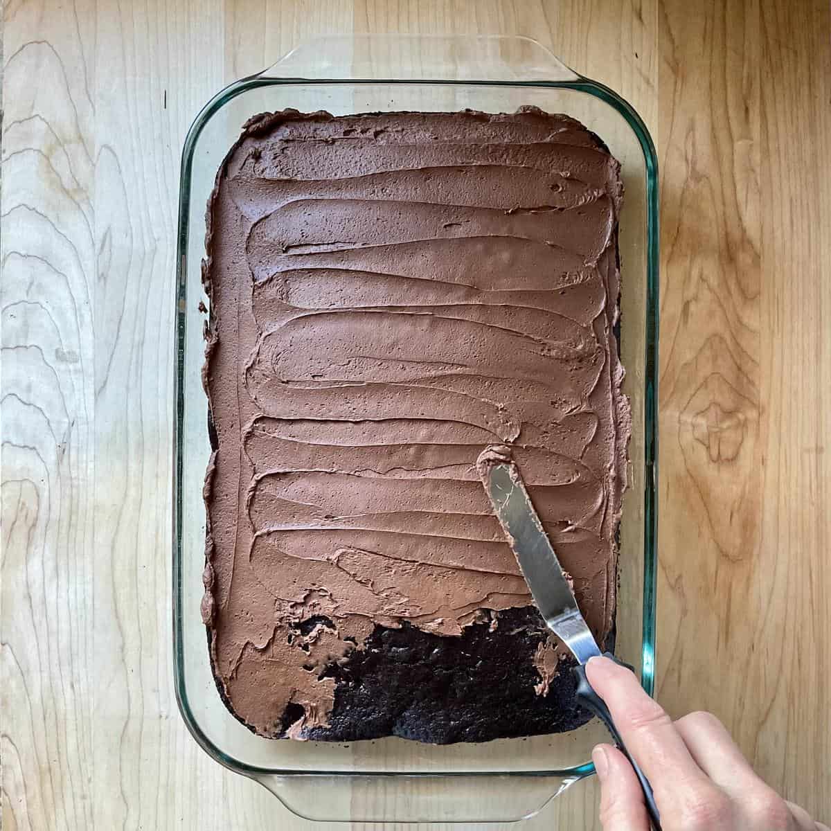 Chocolate frosting being spread over a chocolate cake. 