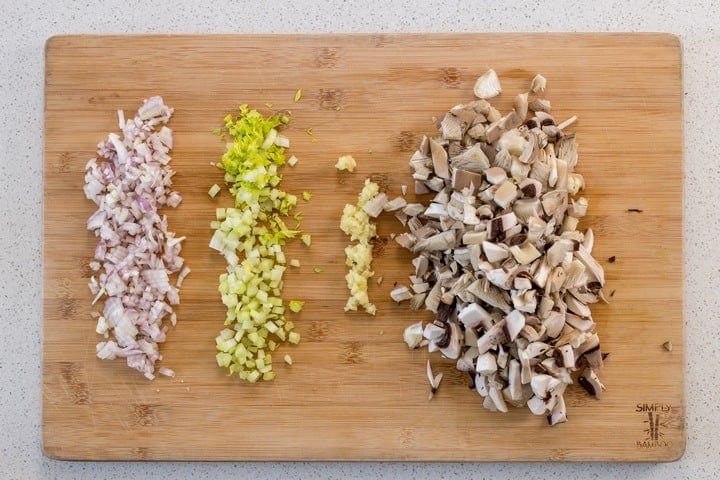 Chopped shallots, celery, garlic and mushrooms on a wooden board.