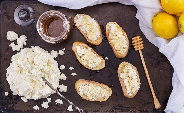 An overhead shot of crostini topped with ricotta cheese and honey.