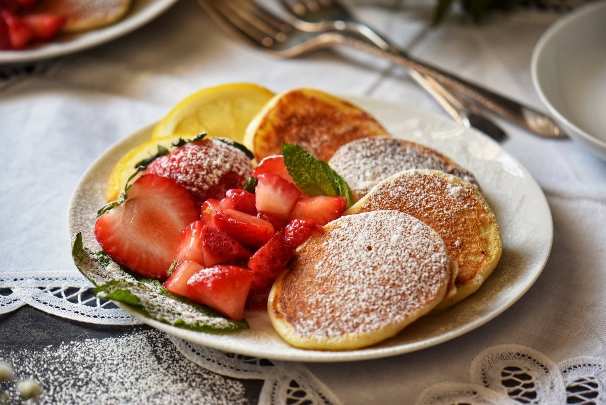 Macerated strawberries next to pancakes in a white plate.