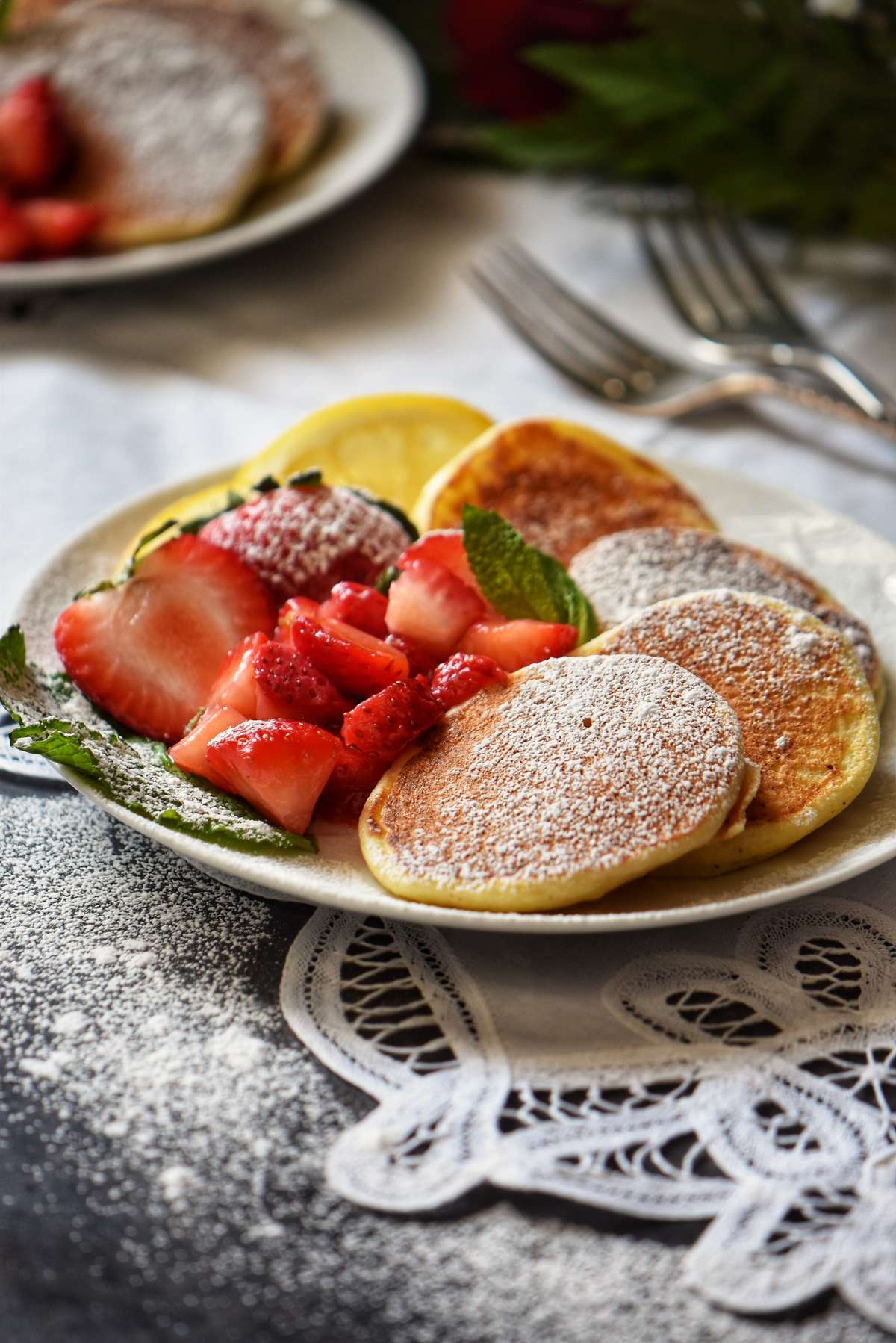 Lemon Ricotta Pancakes in a white plate next to macerated strawberries.