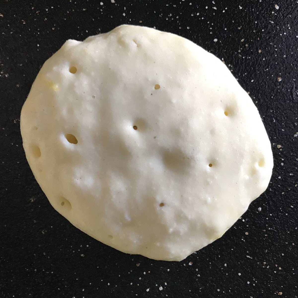 A single pancake on a griddle pan with air bubbles.
