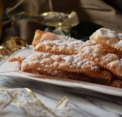 Stacks of crispy crostoli on a white ceramic dish, ready to be served.