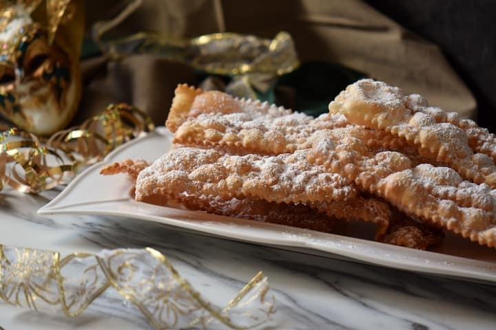 Stacks of crispy crostoli on a white ceramic dish, ready to be served. 