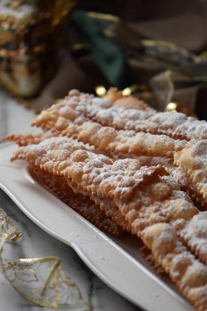 A light and crispy Italian cookie that can be called many names such as crostoli, chiacchiere and angel wings on a white serving platter.