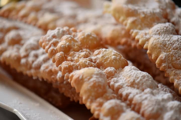 Italian fritters called frappe or crostoli dusted with icing sugar on a white serving platter.