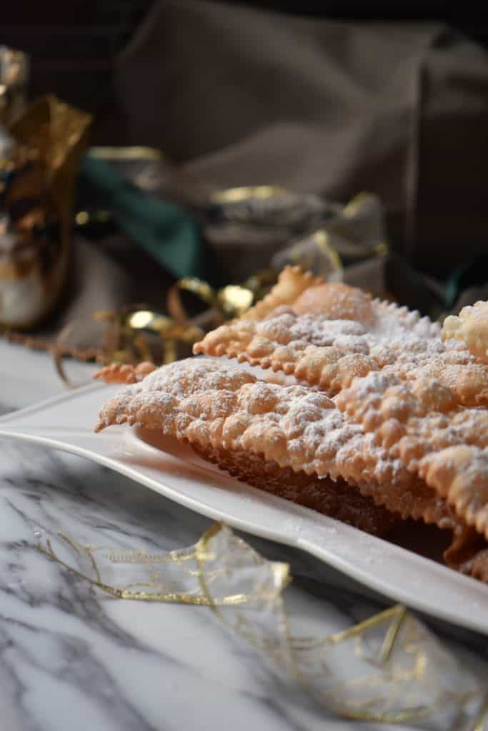 Festive looking crostoli (fried Italian ribbon cookies) on a white serving dish. 