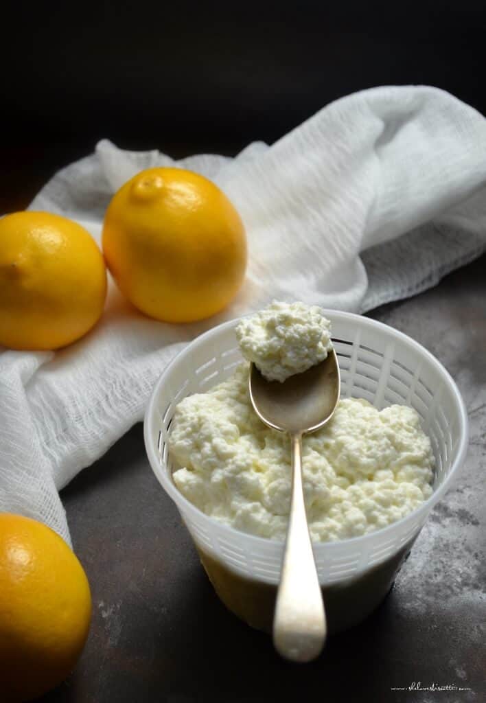 A spoonful of fresh homemade ricotta cheese placed on a cheese basket surrounded by lemons.