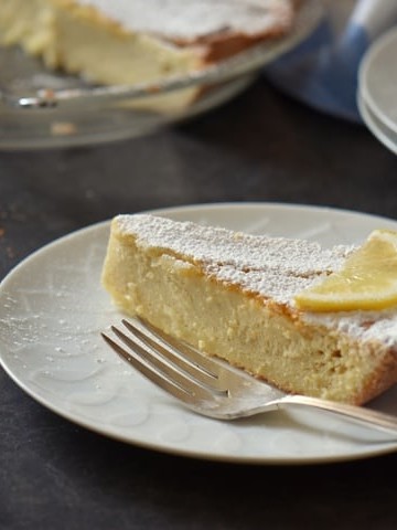 A slice of ricotta pie dusted with icing sugar and decorated with a slice lo lemon.