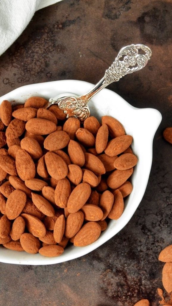 An overhead shot of almond dusted with cocoa powder, in a white bowl.