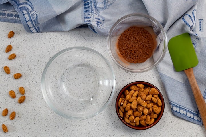 The almonds and the dry ingredients in bowls, surrounded by scattered almonds.