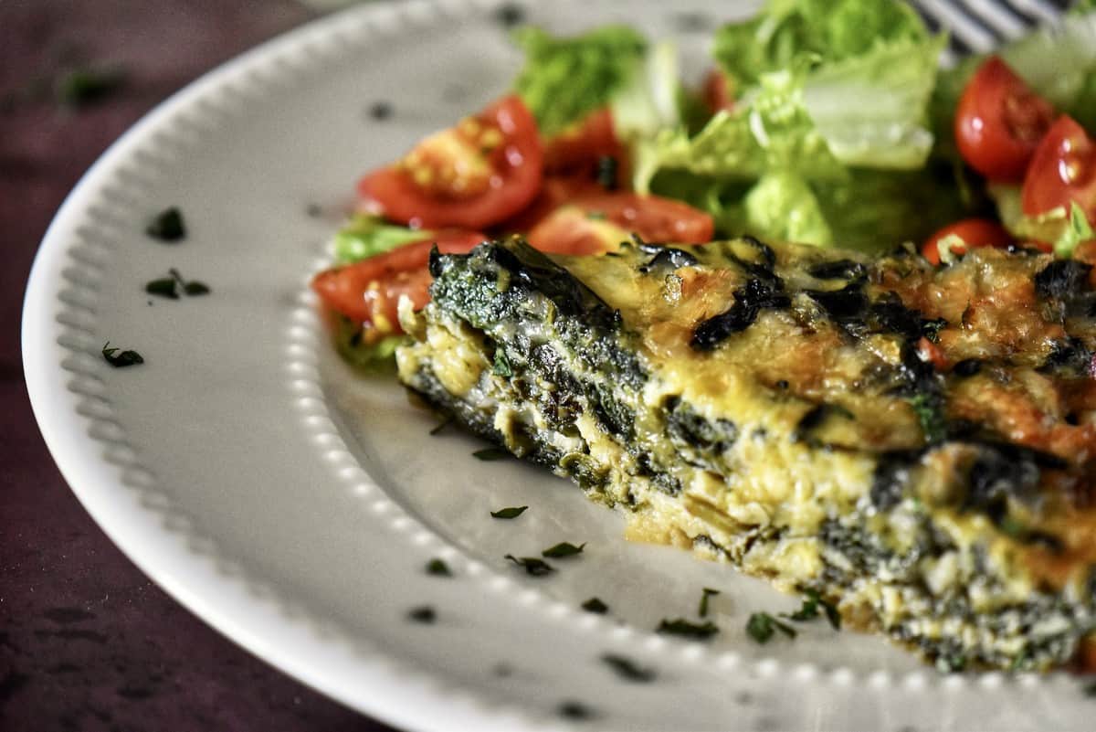 A close-up photo of a slice of spinach quiche on a plate.