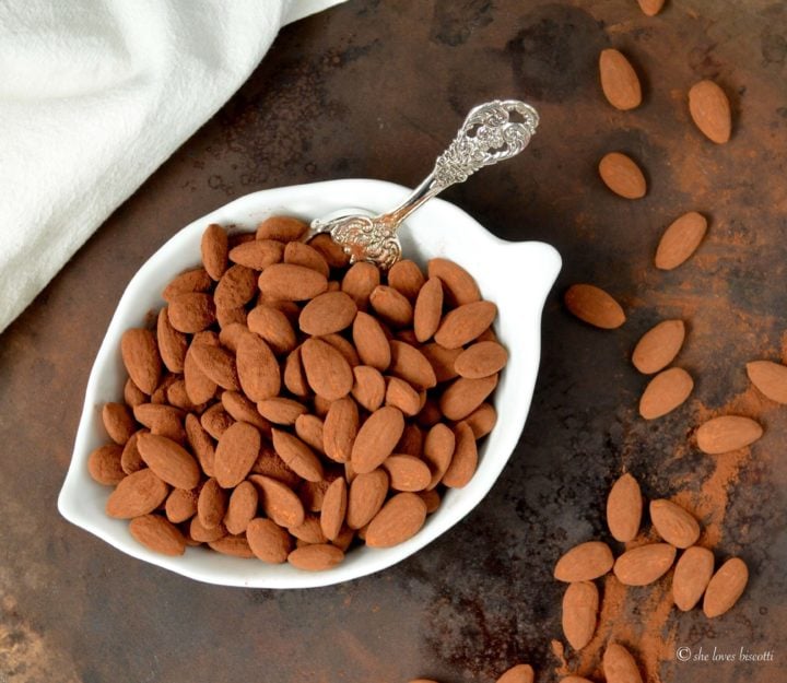 Cocoa Dusted Almonds are shown in a white bowl with almonds scattered on the tray.