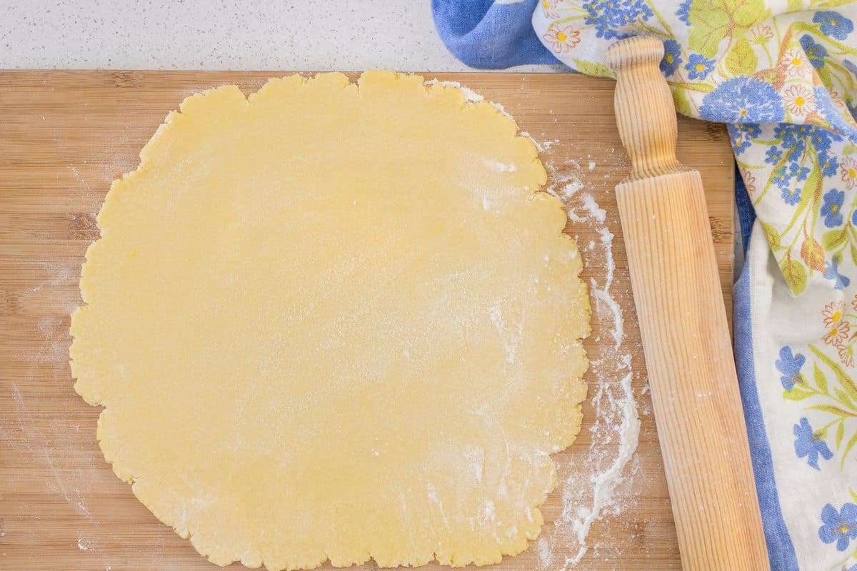 The rolled out dough on a wooden board, next to a rolling pin.