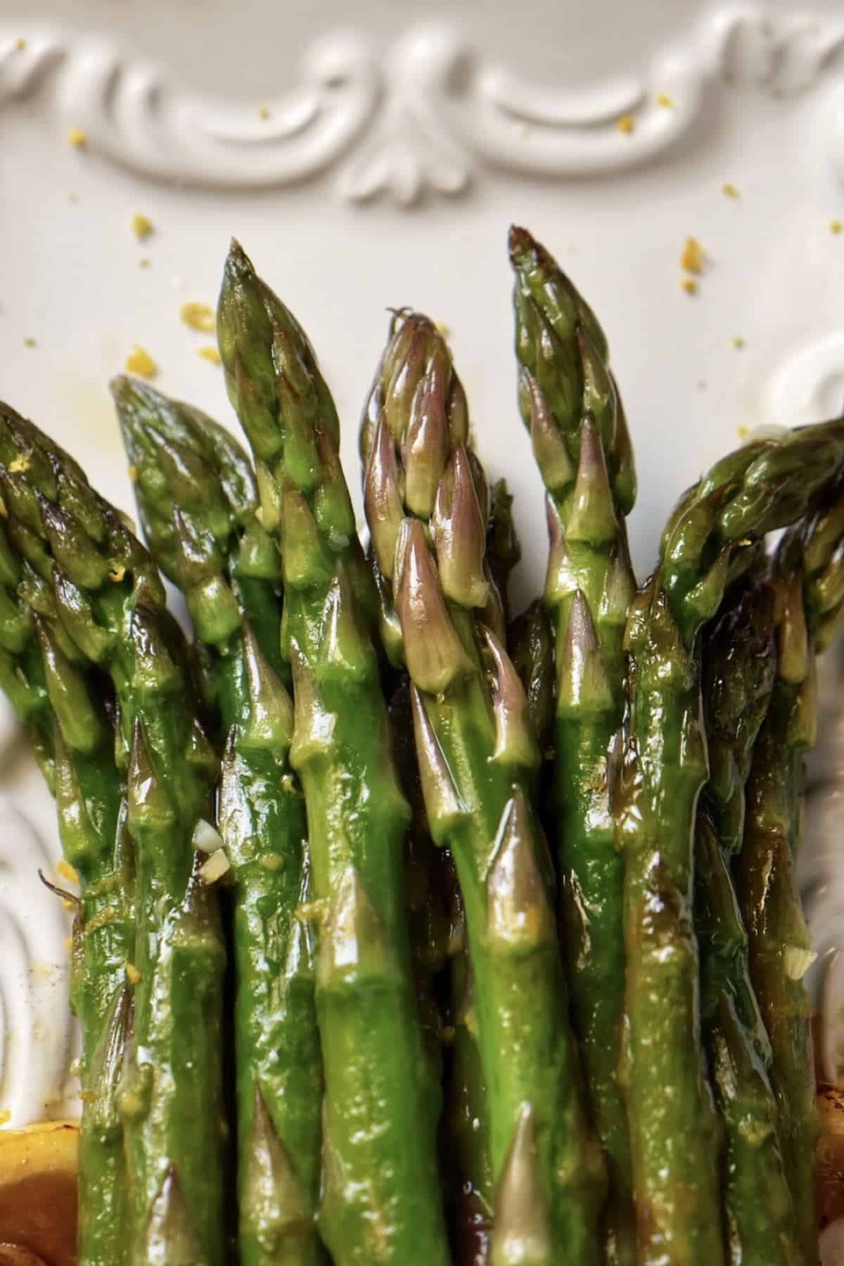 A white platter with lemon and garlic asparagus.