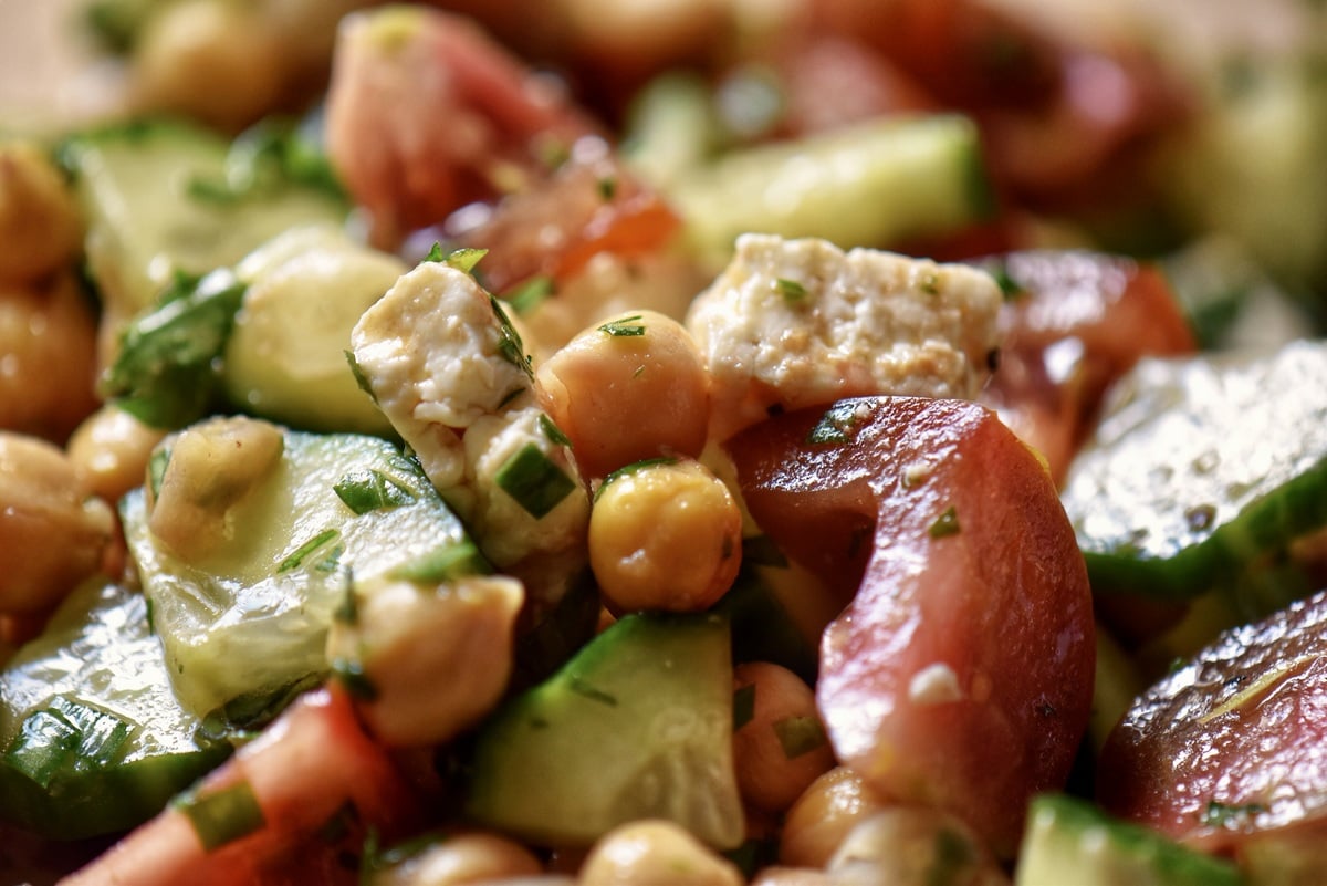 A close up of chickpeas, chopped cucumbers and tomatoes tossed together.