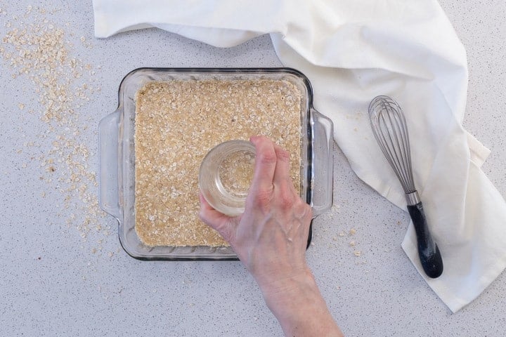 The bottom layer of date squares is being pressed together with a heavy bottomed glass.