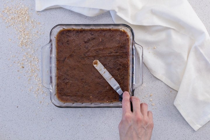 The date filling is being spread over the oat crumble mixture.