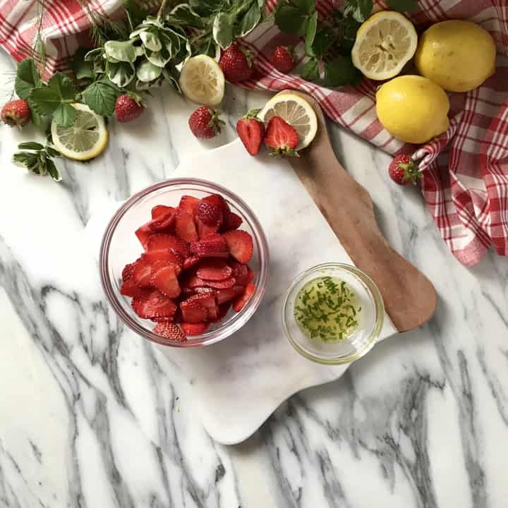 A bowl of sliced strawberries next to a bowl of the marinade.