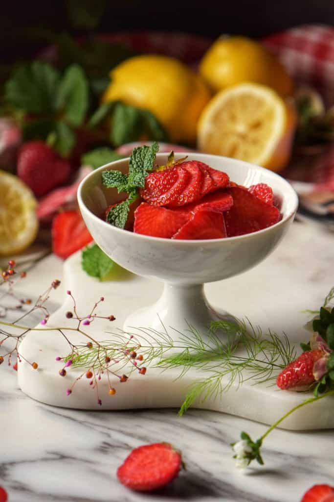 Sweetened strawberries in a white dish, surrounded by fresh strawberries. in a white dish, surrounded by fresh strawberries.