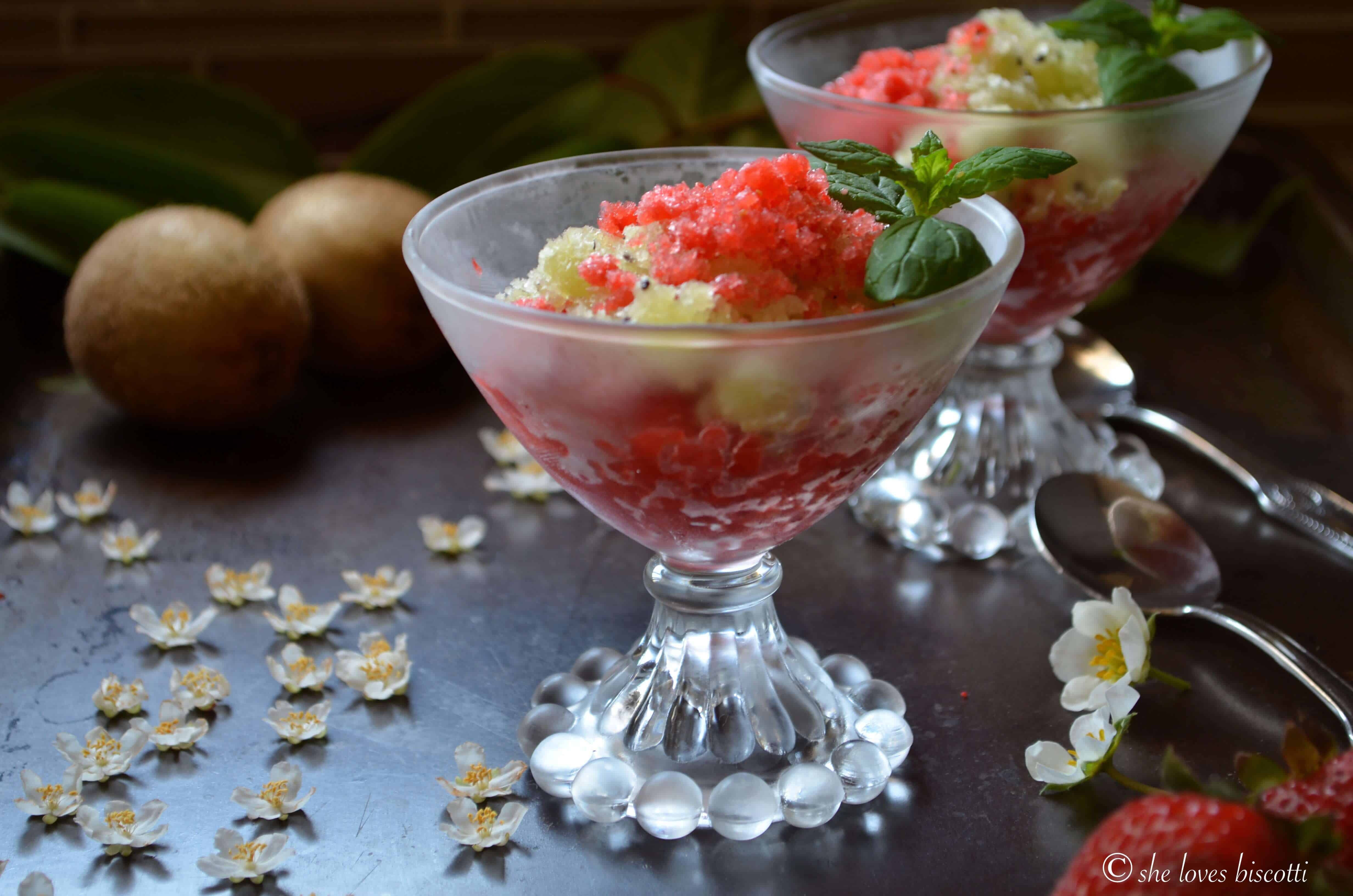 Kiwi granita in a bowl surrounded by kiwi flowers, kiwis and strawberries.