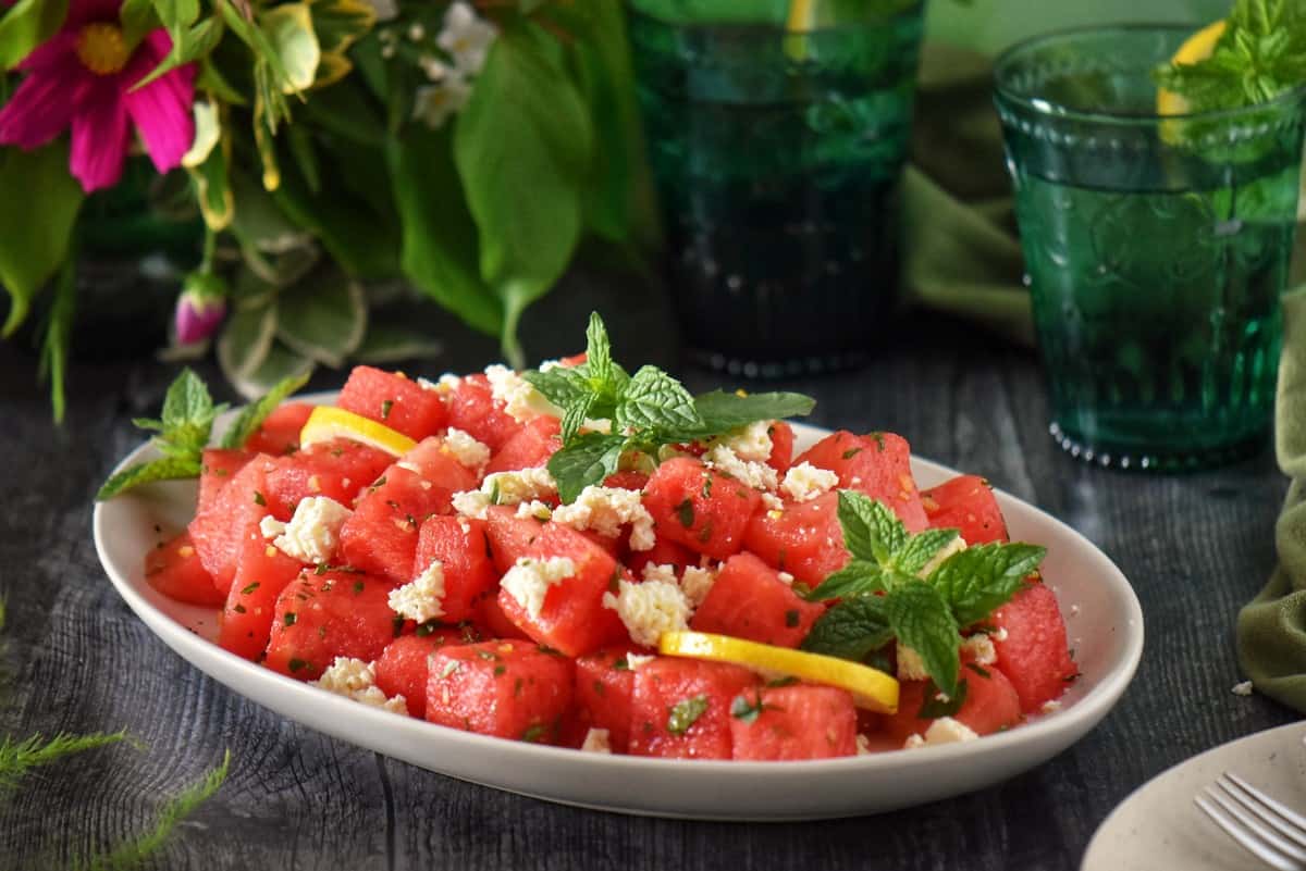 Cubes of watermelon on a white plate garnished with a lemon vinaigrette.