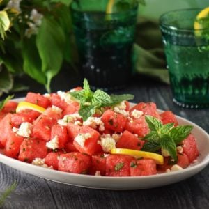 Watermelon salad garnished with feta and mint on a large white platter.