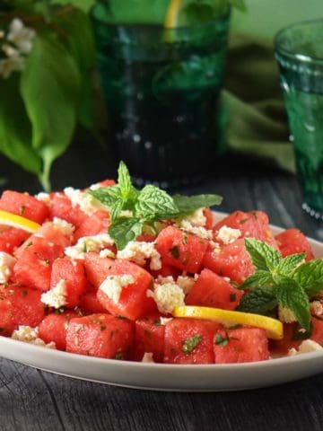 Watermelon salad garnished with feta and mint on a large white platter.