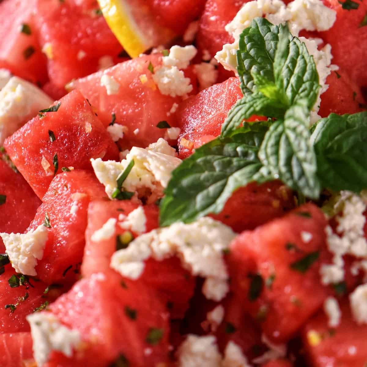 A close up photo of a refreshing watermelon salad topped with feta and mint leaves.