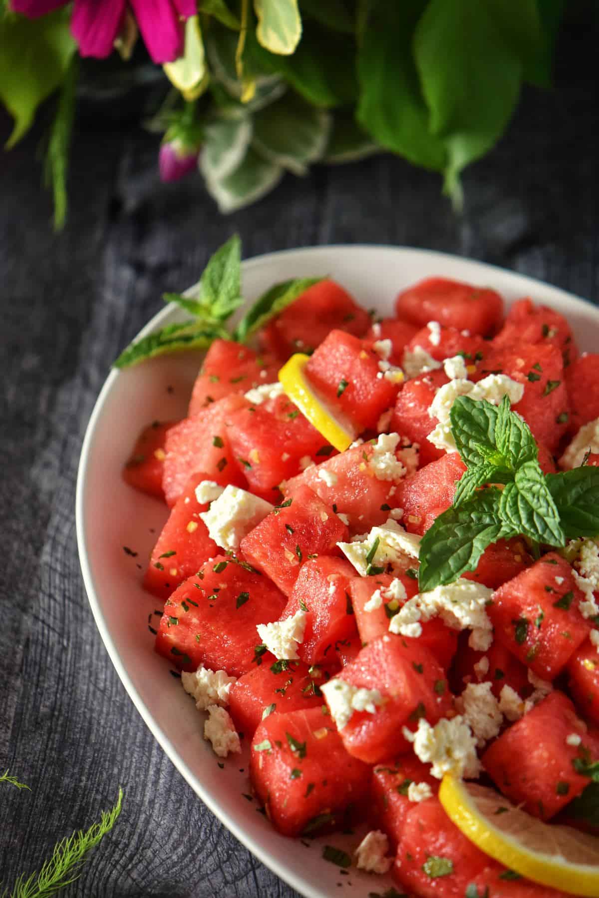 Watermelon and feta salad on a white plate garnished with mint and lemon. 