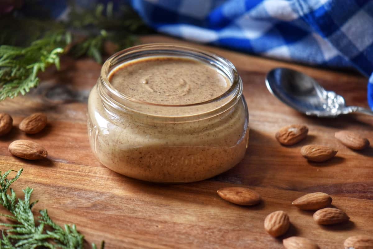 An overhead photo of almond butter in a jar, next to almonds.