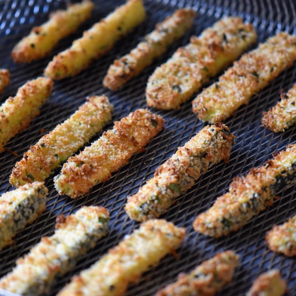 Baked zucchini fries on an air fryer basket.